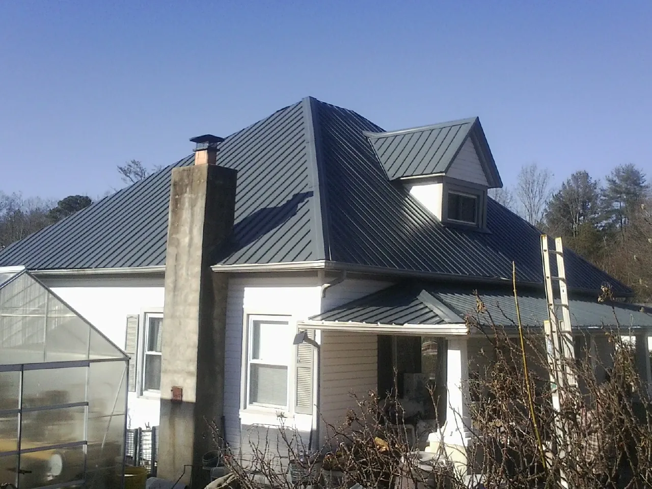 Dark blue standing seam metal roof on a white farmhouse with dormer — Slate & Tile Roof Repair by Roofing Brothers in Avery