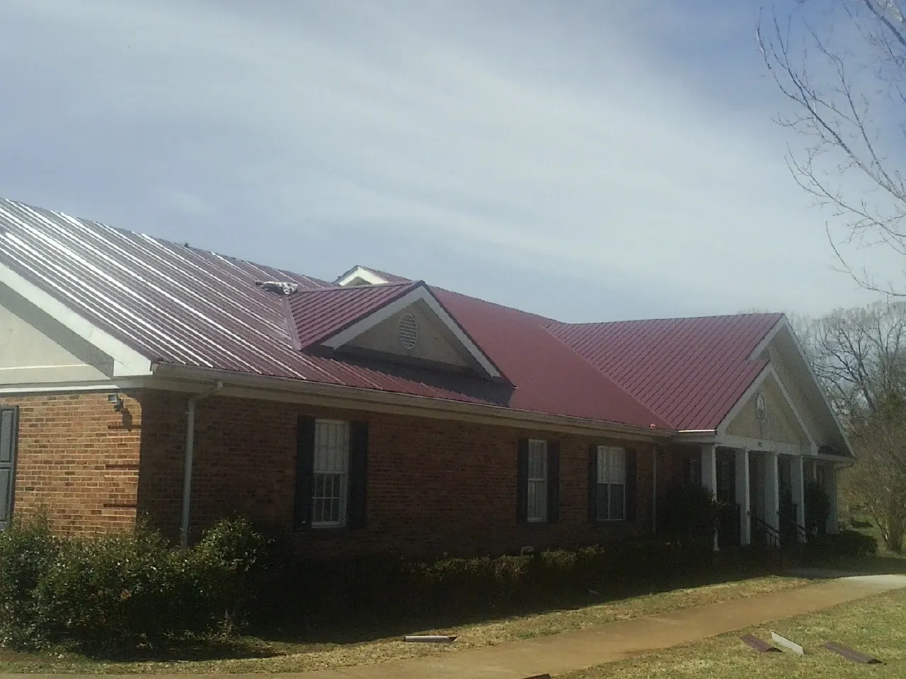 Red metal roof with gabled entries on a long brick building, from a Hail Damage Roof Repair job in Avery