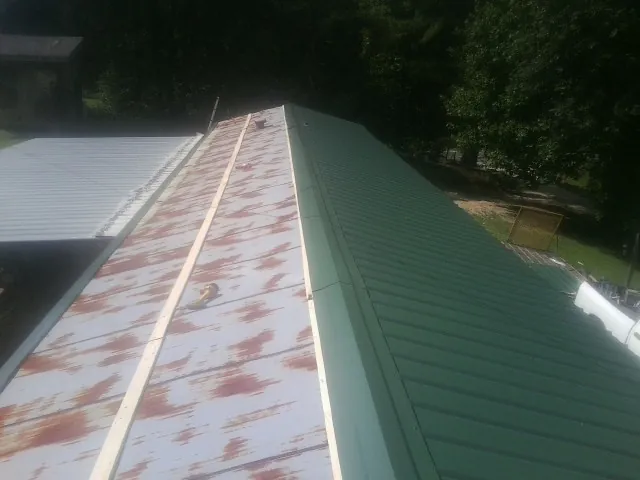 Old rusted panels beside newly installed green metal roofing — Wind Damage Roof Repair by Roofing Brothers in Avery