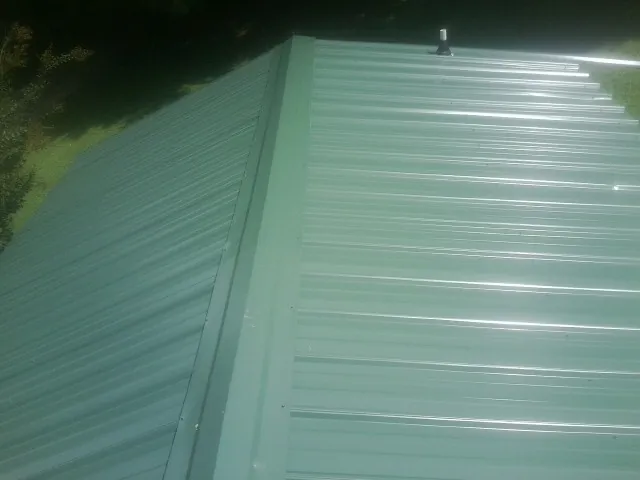 New green metal panels meeting at the ridge of a roof — Flat Roof Repair work by our crew in Avery