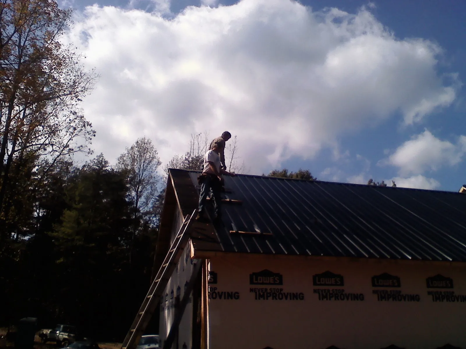 Roofer fastening dark metal panels high against a cloudy sky, from a Roof Inspection job in Avery